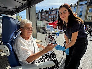 Seniorenmesse_1.jpg Eine ältere Frau sitzt in einem Rollstuhl. Eine dunkelhaarige jüngere Frau misst den Blutzucker.